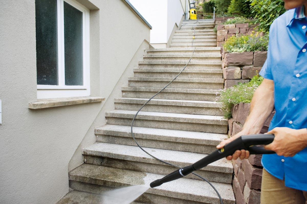 Prodloužení vysokotlaké hadice 6m pro K 3 - K 7 od společnosti Karcher. Muž myjící schody. Mezi pistolí a čističem je připojeno prodloužení vysokotlaké hadice.