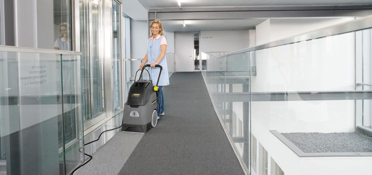Profesionální, kompaktní zařízení pro základní čištění BRC 30/15 C od firmy Karcher Profesionální, kompaktní zařízení pro základní čištění BRC 30/15 C od firmy Karcher. Žena extrakčně čistící podlahový koberec na chodbě v kancelářské budově.