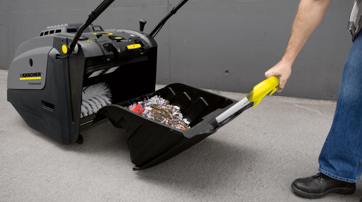 Profesionální ruční zametací stroj KM 75/40 W Bp od Karcher s elektrickým motorem. Muž vytahující nádrž na nečistoty z profesionálního zametacího stroje KM 75/40 W Bp vyráběného firmou Karcher.